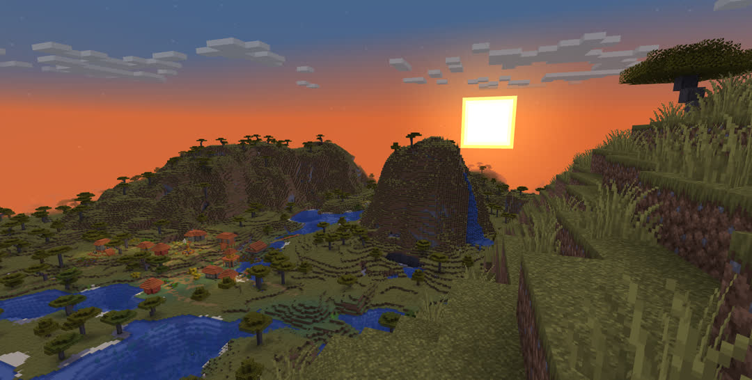 A river valley between a pair of savanna plateaus at sunset. A village is settled along the river at the foot of one of the plateaus.