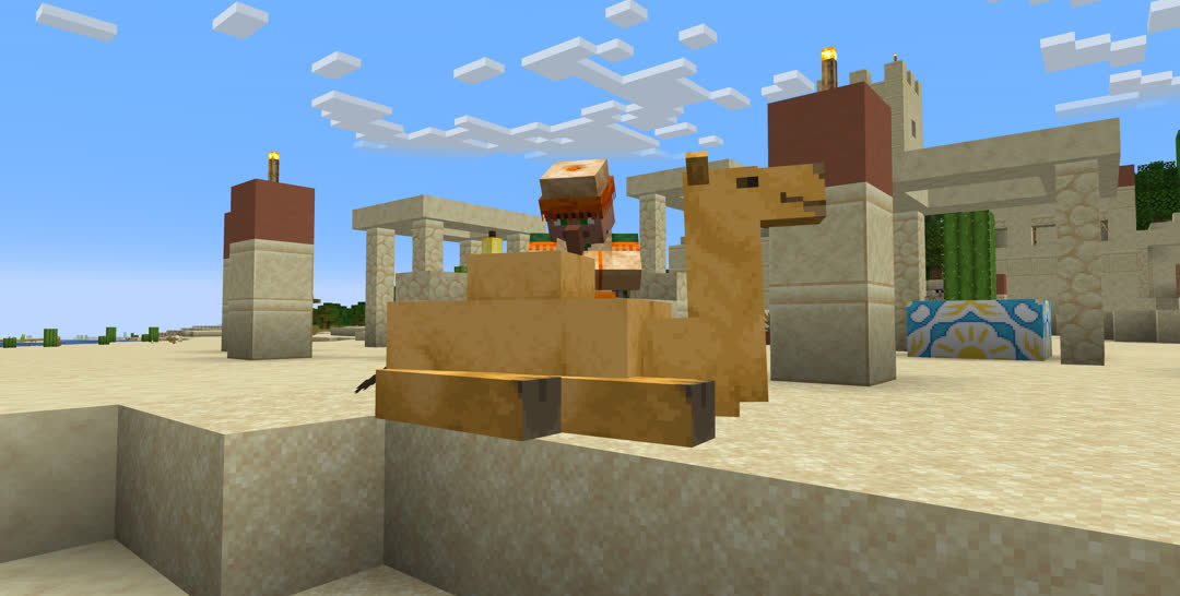 A camel laying down on the sand near the center of a desert village. One villager is standing next to and looking down at it.